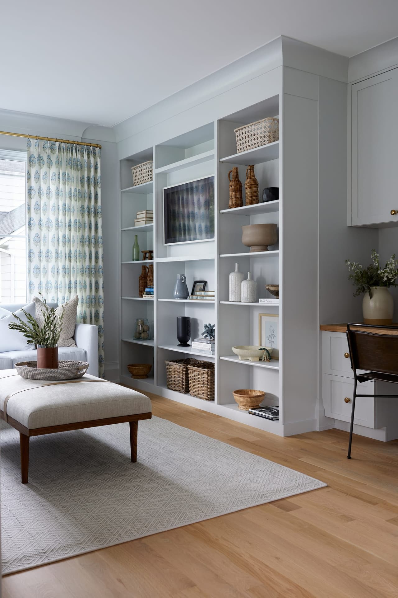 Built-in white shelving and a desk nook beside the window of a Westfield, NJ new-construction home, with an upholstered bench on a pale rug