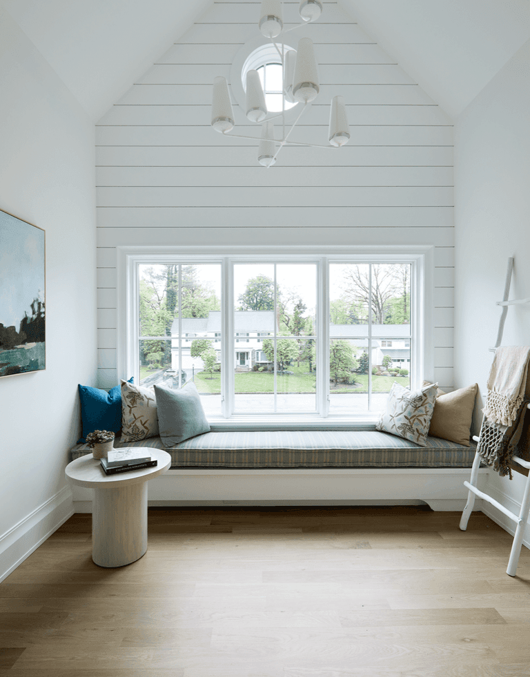 Window-seat banquette under a vaulted shiplap gable, with a three-panel window, a white chandelier and white oak floors
