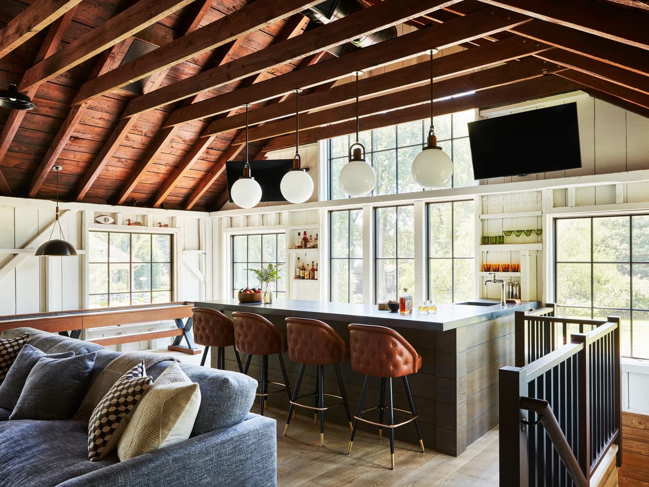 Barn interior under an exposed stained-timber roof, with a full bar, leather stools and a sectional