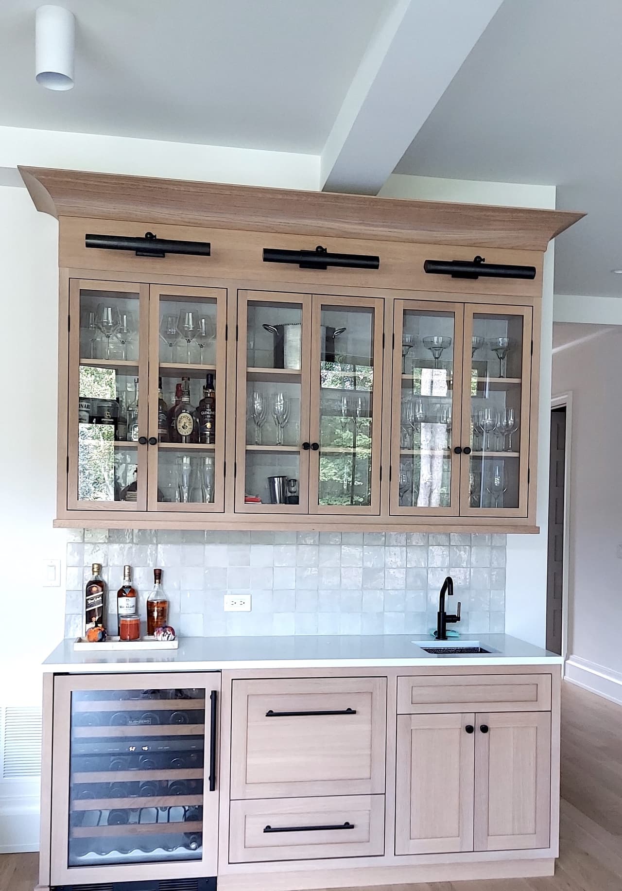 Custom bar in a Westfield, NJ new-construction home, with glass-front upper cabinets on sliding hardware, a pale pink base and a beverage fridge