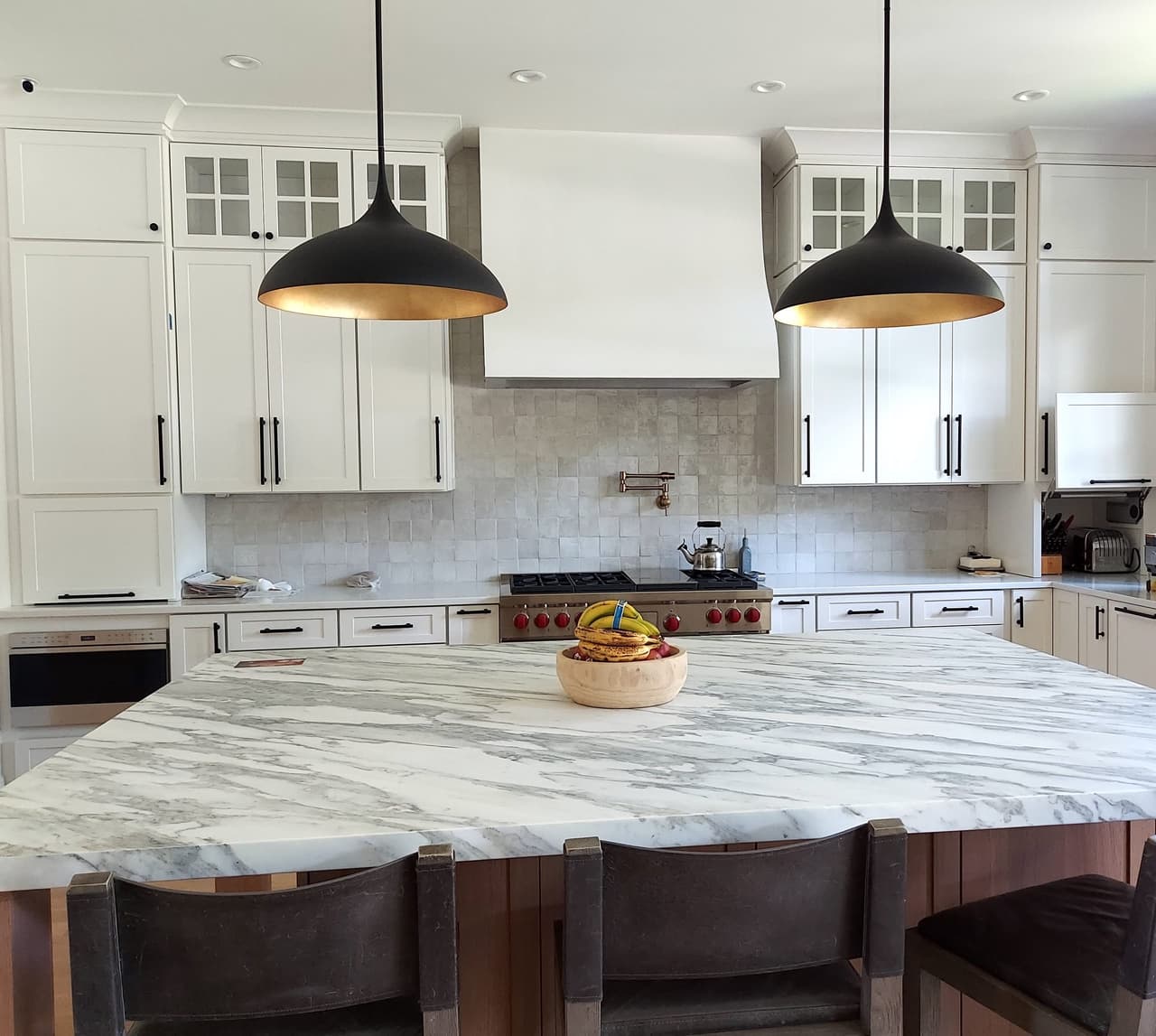 Kitchen in a Westfield, NJ new-construction home, with a plaster hood, black dome pendants, marble counters and a large island with leather stools