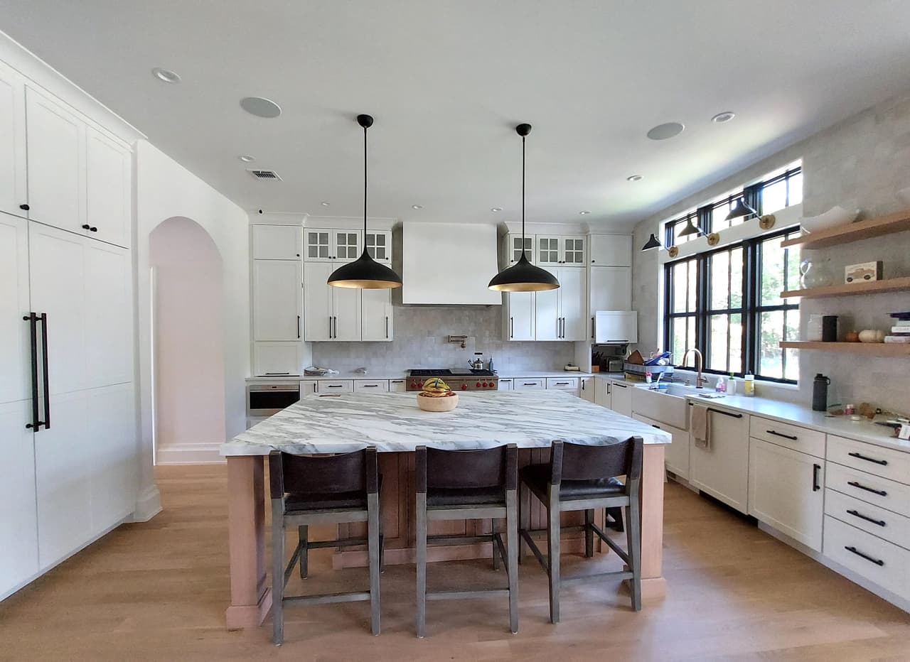 Kitchen and island in a Westfield, NJ new-construction home, with black dome pendants, an arched cased opening and a window wall along the counter