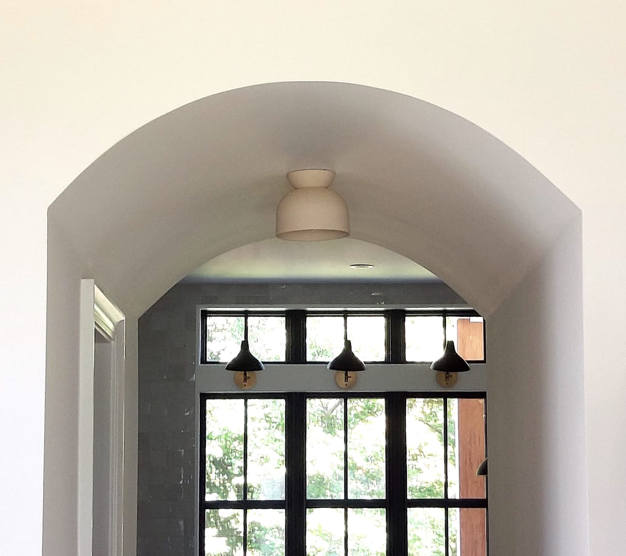 Plaster archway in a Westfield, NJ new-construction home framing a black steel window with three picture lights above it