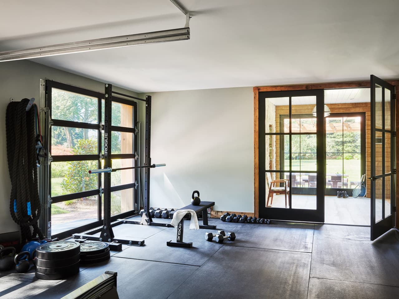 Gym in a Westfield, NJ historic barn renovation, with rubber flooring, a rack of plates and black steel doors through to the hall