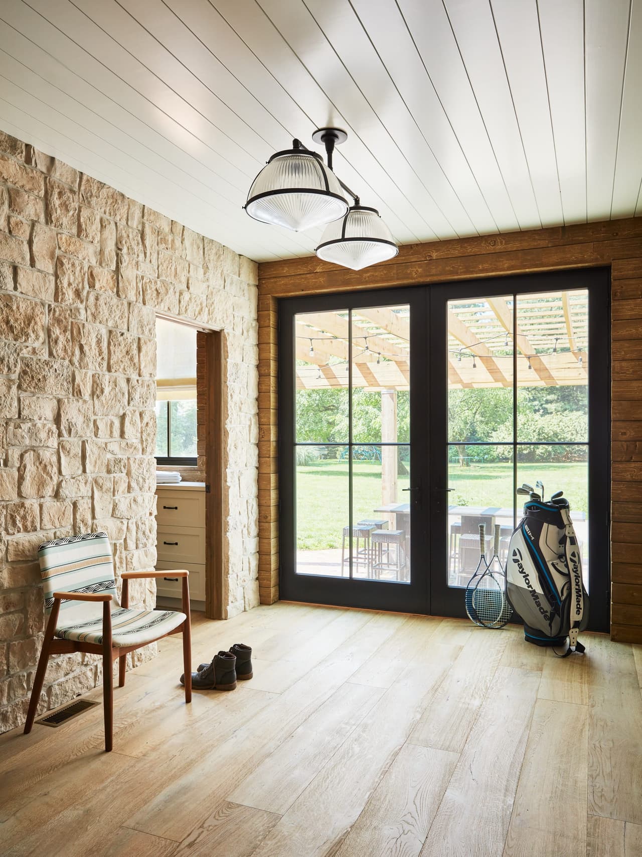 Hallway of a Westfield, NJ historic barn renovation, with an exposed stone wall, a planked ceiling and glazed doors onto the lawn
