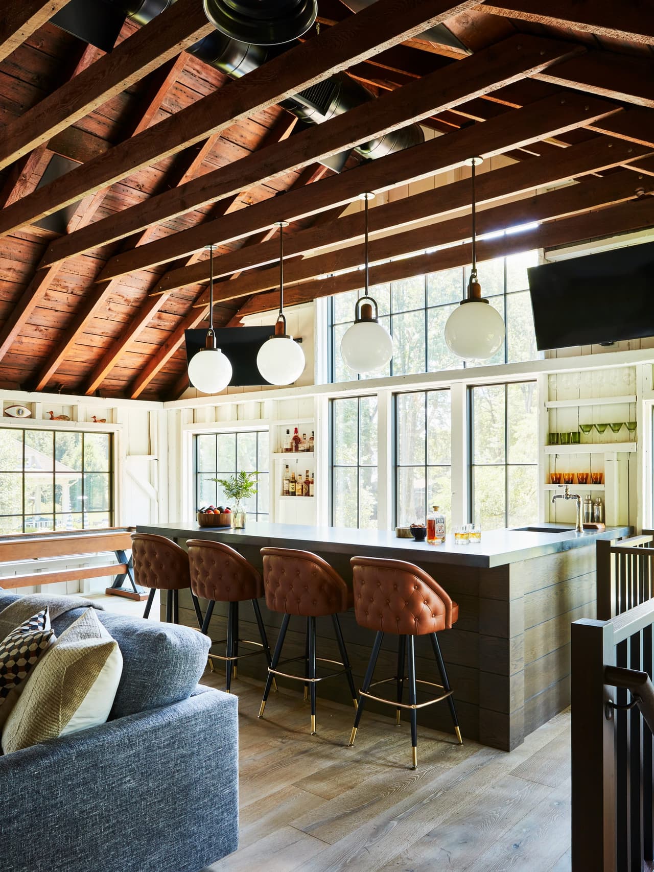Bar and leather counter stools under the exposed rafters of a Westfield, NJ historic barn renovation, with globe pendants hung from the collar ties
