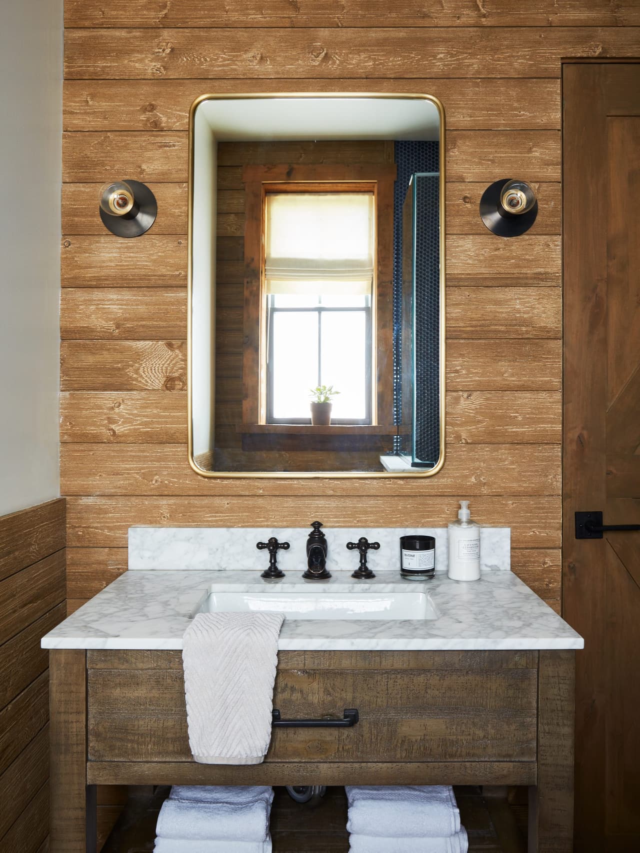 Bathroom in a Westfield, NJ barn renovation, with reclaimed wood walls, a marble-topped washstand and a black-framed mirror between two sconces