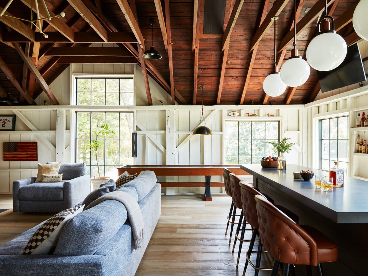 Side view across the family space of a Westfield, NJ barn renovation, from the sectional past the long table to the bar and leather stools