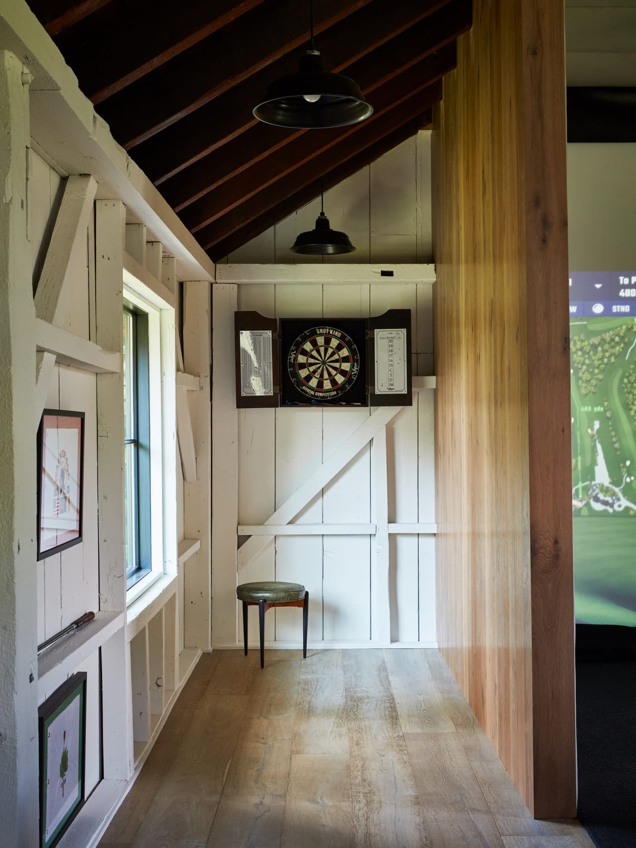 Game space in the barn with board-and-batten walls, a dartboard in a cabinet and an exposed rafter ceiling