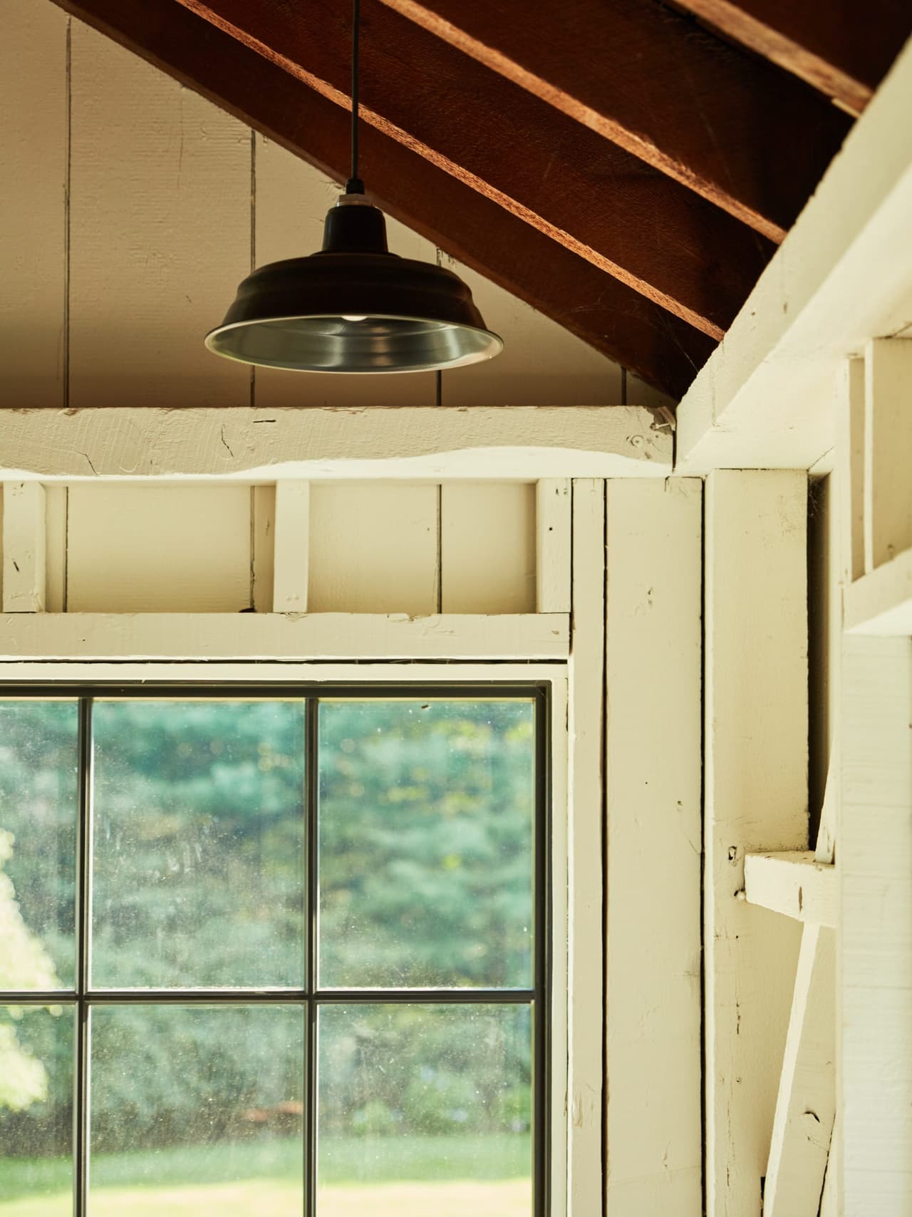 Plank siding and a gooseneck barn light where the roof meets the wall inside a Westfield, NJ historic barn renovation, above a black-framed window