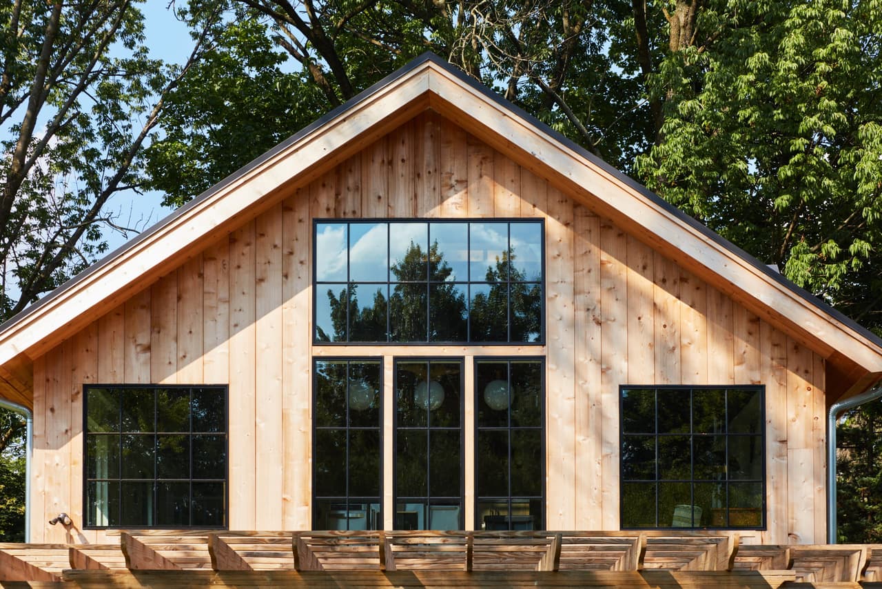 Gable end of a Westfield, NJ historic barn renovation, clad in vertical cedar with a stack of black-framed windows filling the peak, by Michael Robert Construction