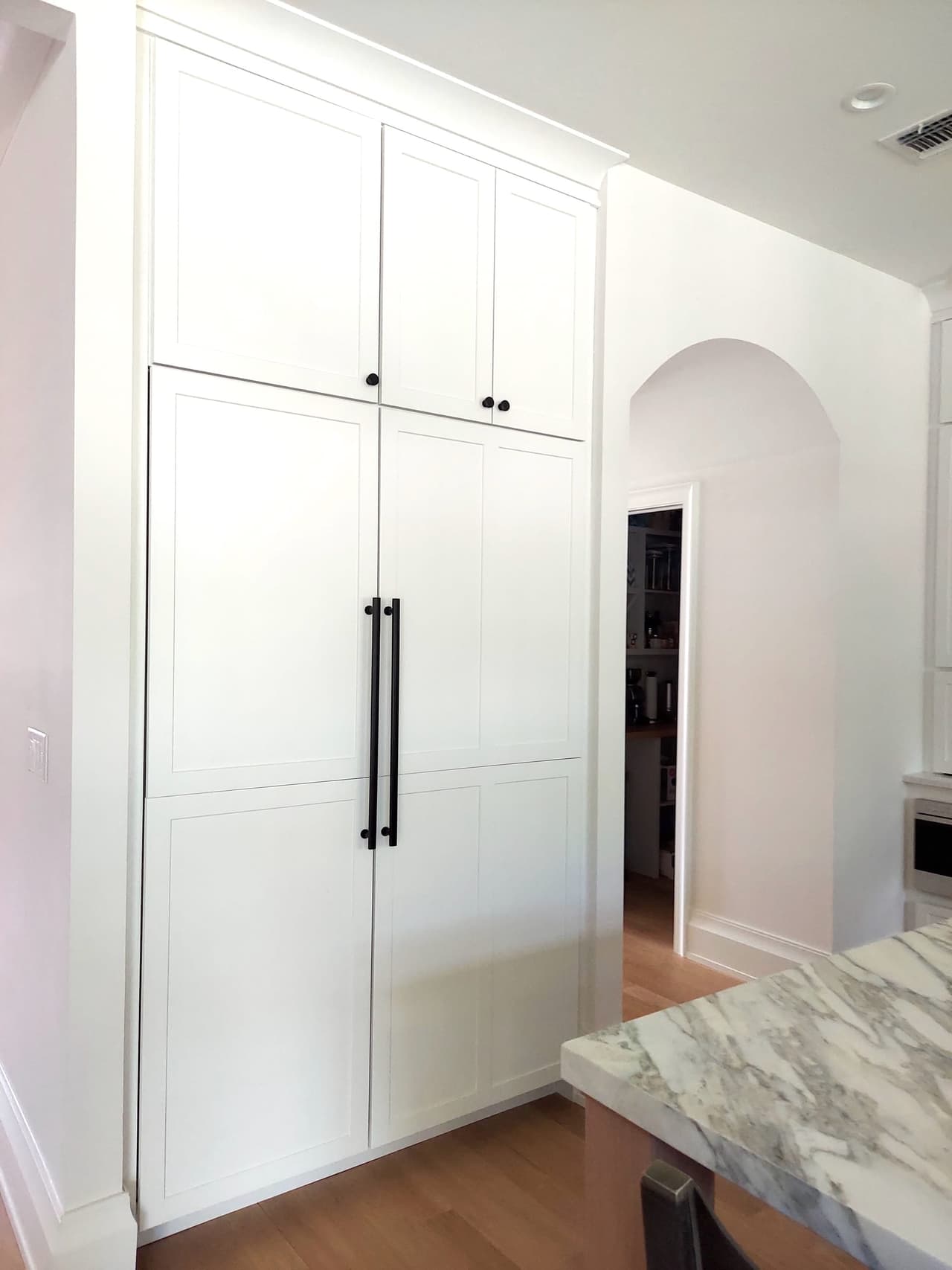 Full-height white kitchen cabinetry with long black pulls beside a marble counter in a Westfield, NJ new-construction home, with an arched opening to the hall
