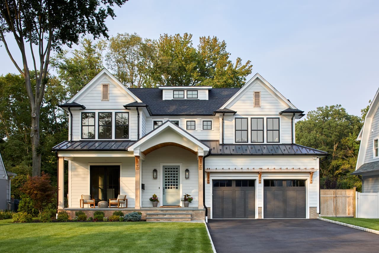 Front of a Westfield, NJ new-construction home with a pale blue door, cedar accents, a standing-seam porch roof and dark garage doors
