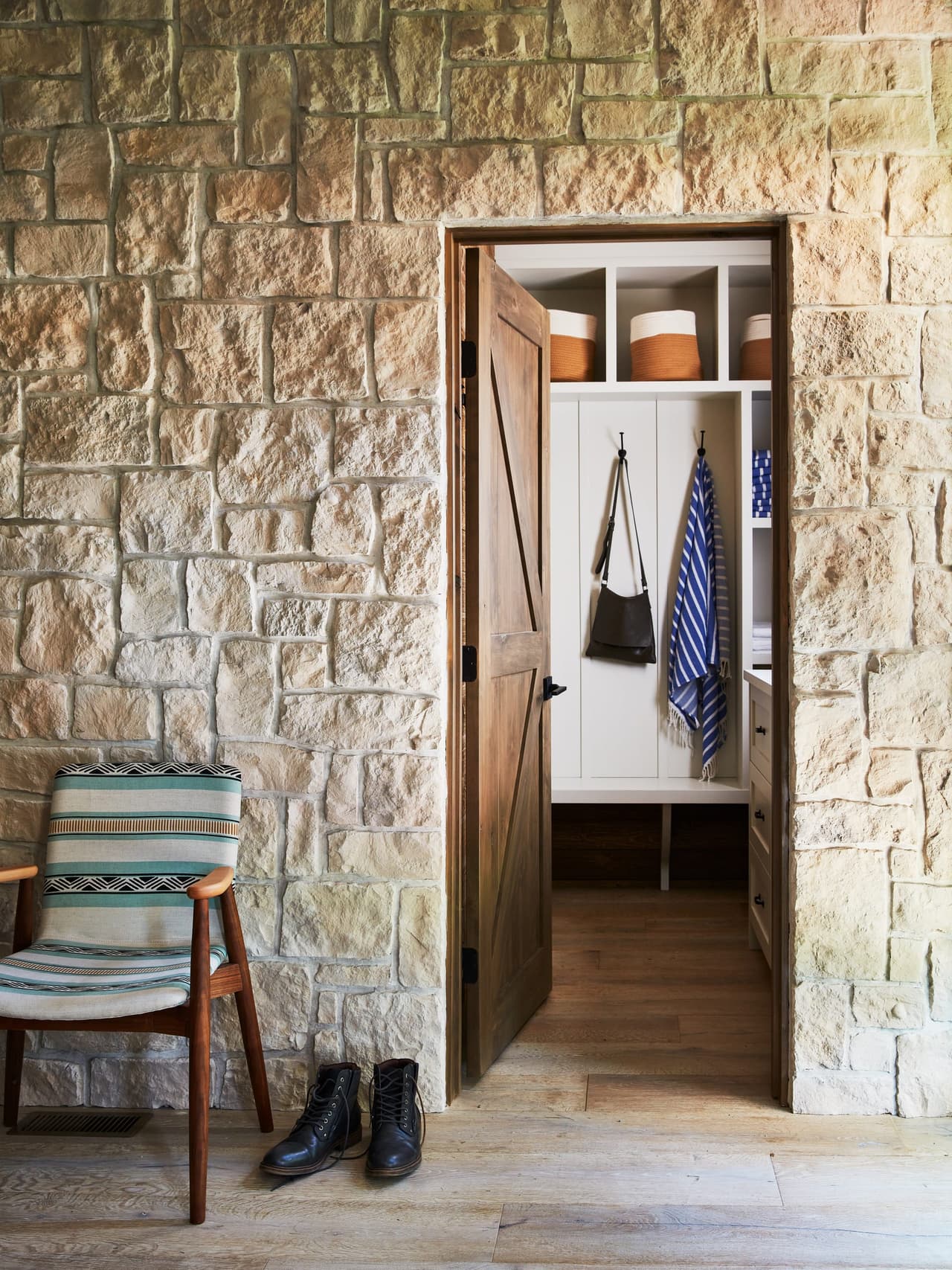 Stone wall and plank door opening to a mudroom with hooks and shelving, beside a bench