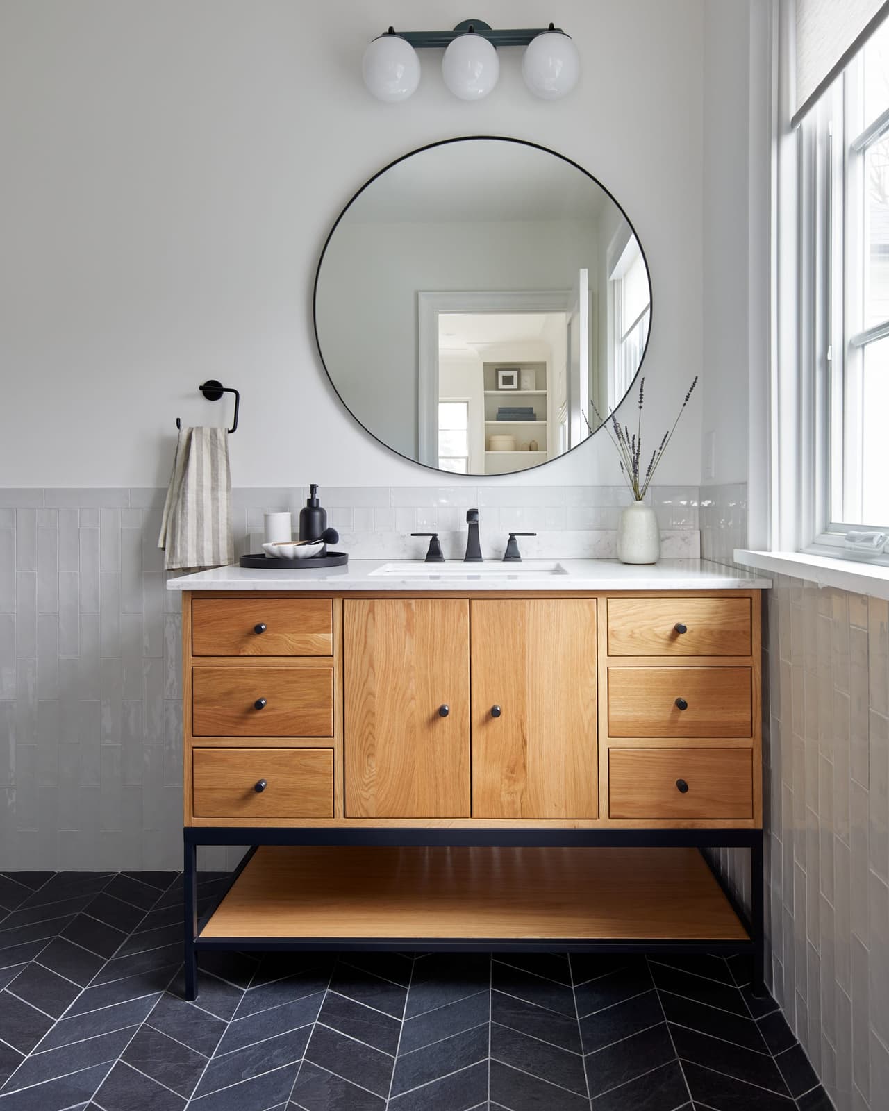 Bathroom in a Westfield, NJ addition and whole-home renovation, with a white oak vanity on a black metal frame, a round mirror and a herringbone slate floor