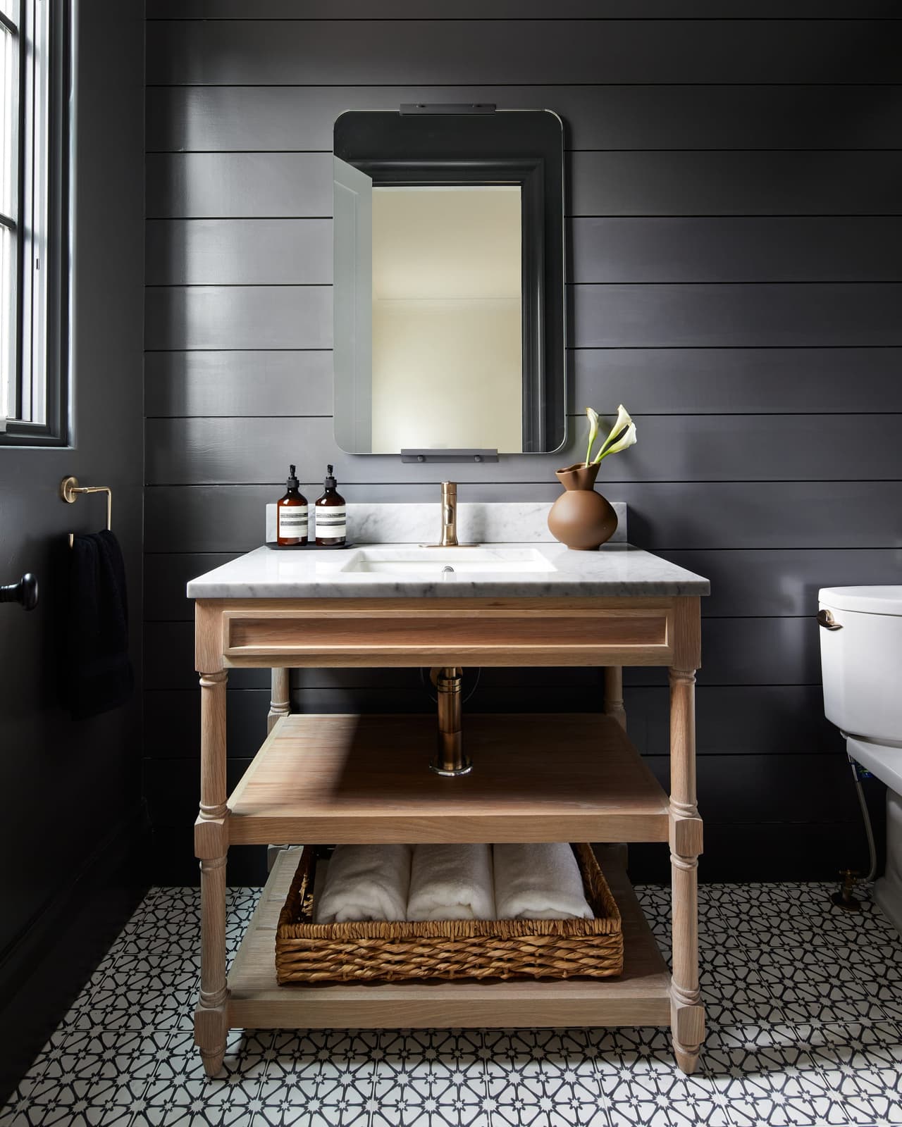 Guest bathroom in a Westfield, NJ addition and renovation, with black shiplap walls, a wood washstand under a marble top and a pebble mosaic floor