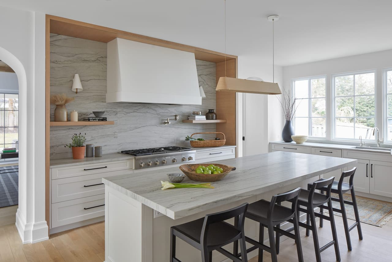Plaster hood in an oak surround over the range, facing a long quartzite island with black stools, in a Westfield, NJ addition and renovation