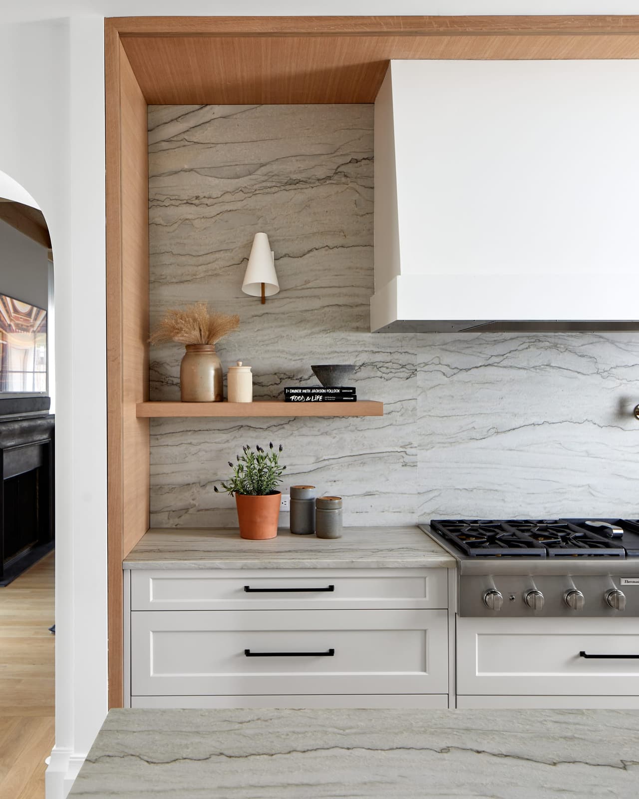 Range wall of a Westfield, NJ kitchen, with the quartzite slab run up behind the cooktop, an oak shelf across it and the hood framed in oak
