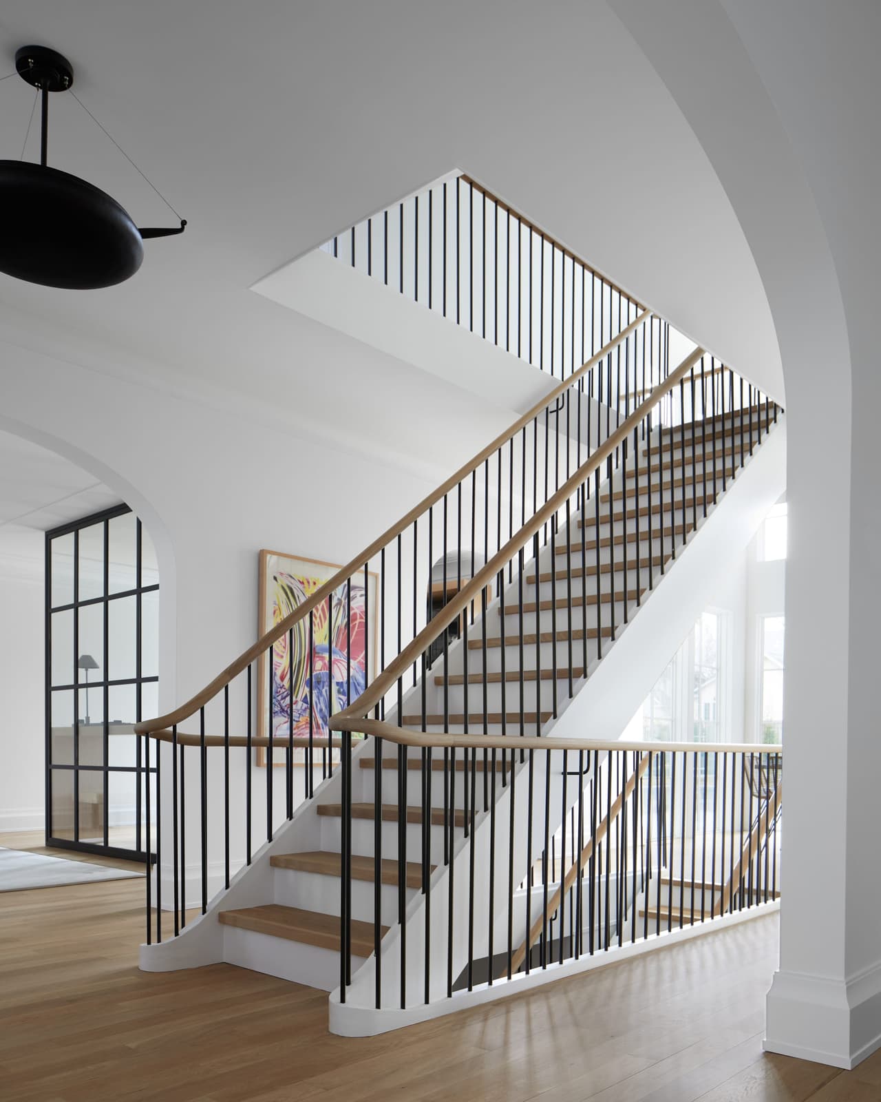 Stair of a Westfield, NJ whole-home addition and renovation, with oak treads, a wood handrail over thin metal balusters and an arched opening at the foot