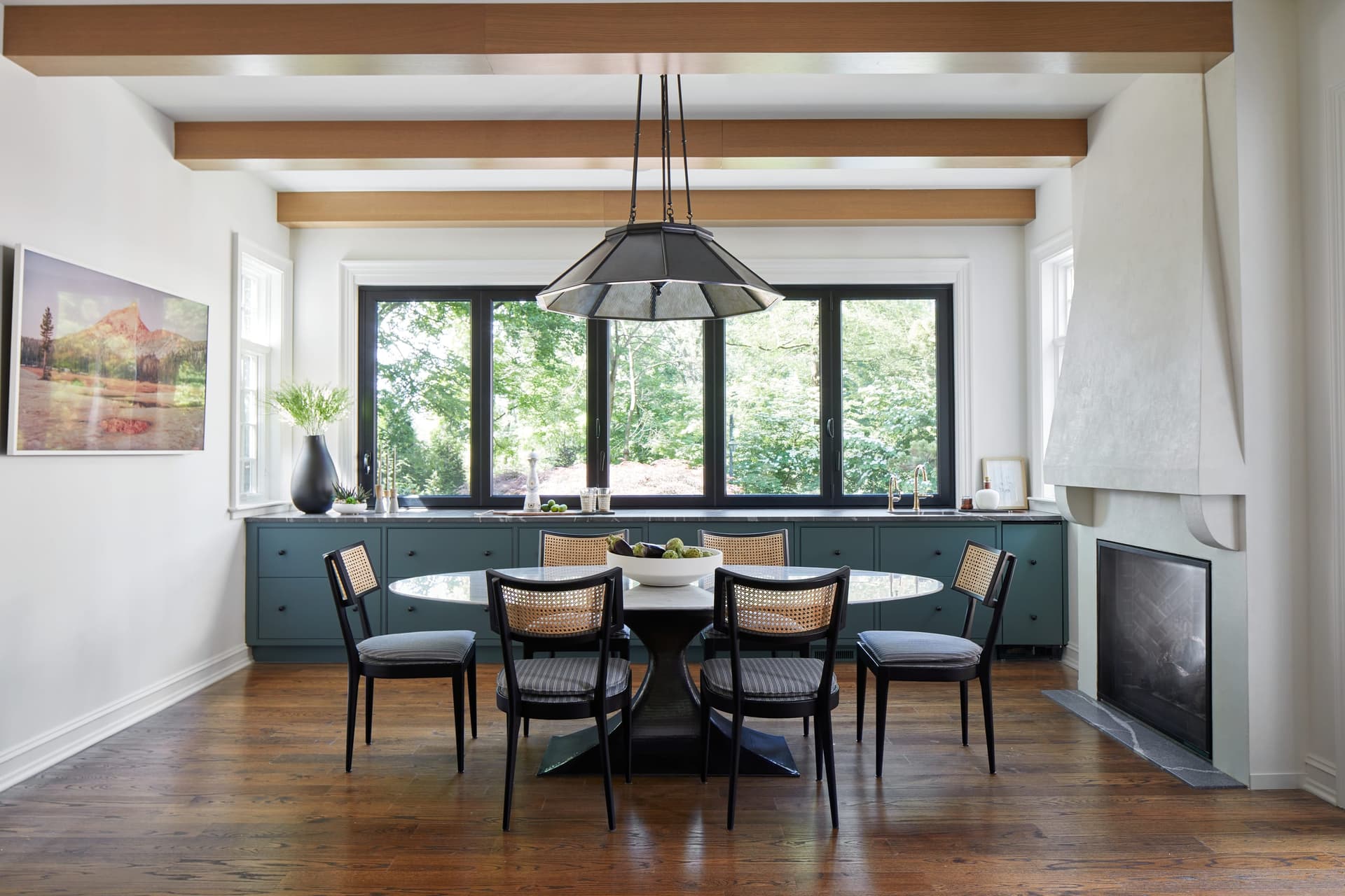 Eating area beside the fireplace in a Westfield, NJ kitchen renovation, with a linear chandelier over the table and black steel doors to the terrace