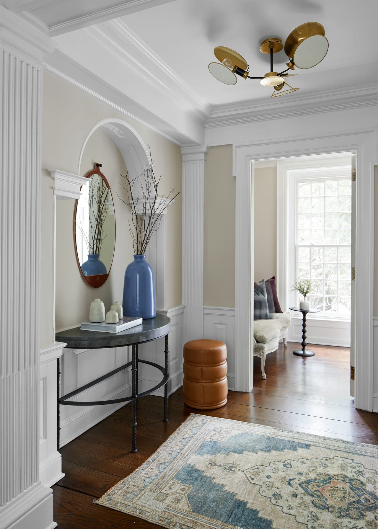 Front entry and foyer of a Westfield, NJ home renovation, with paneled wainscot, an arched niche, a demilune table and a view through to the sitting room