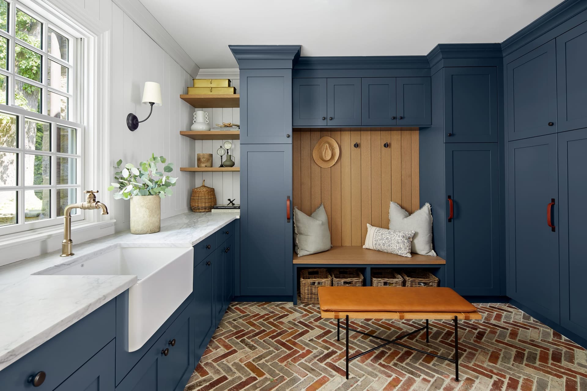 Mudroom with navy blue cabinetry in a Westfield, NJ home renovation, with an apron-front sink, an oak bench between lockers and a herringbone brick floor