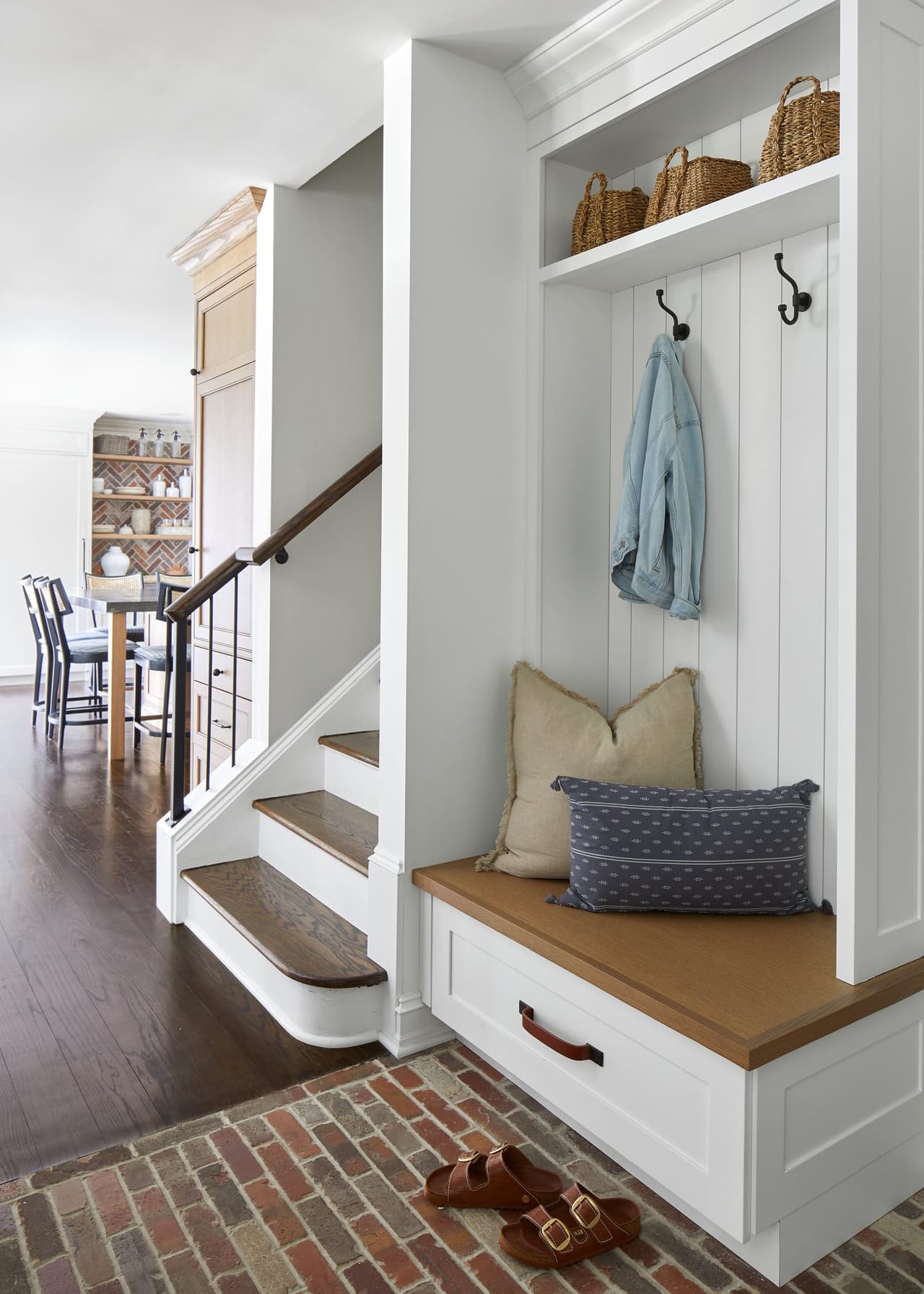 Built-in bench and coat hooks tucked under the stair of a Westfield, NJ home renovation, on a brick floor