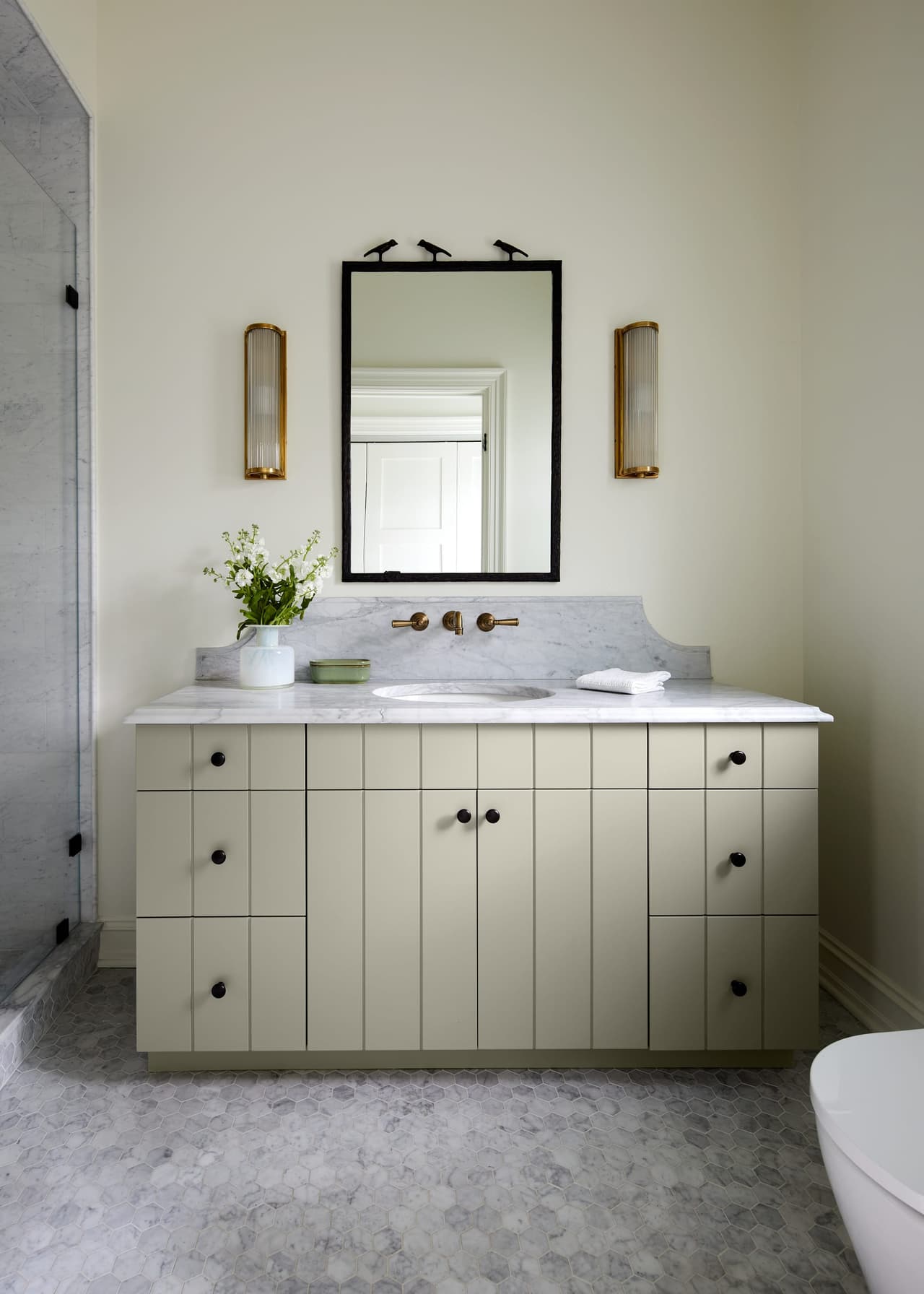 Powder room of a Westfield, NJ home renovation with a fluted vanity, a marble top and a black-framed mirror between two sconces