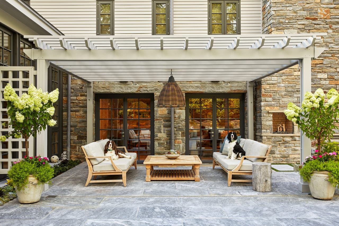 Dog asleep on the sofa under a pergola off the stone rear elevation of a Westfield, NJ home, with teak seating and hydrangeas in pots