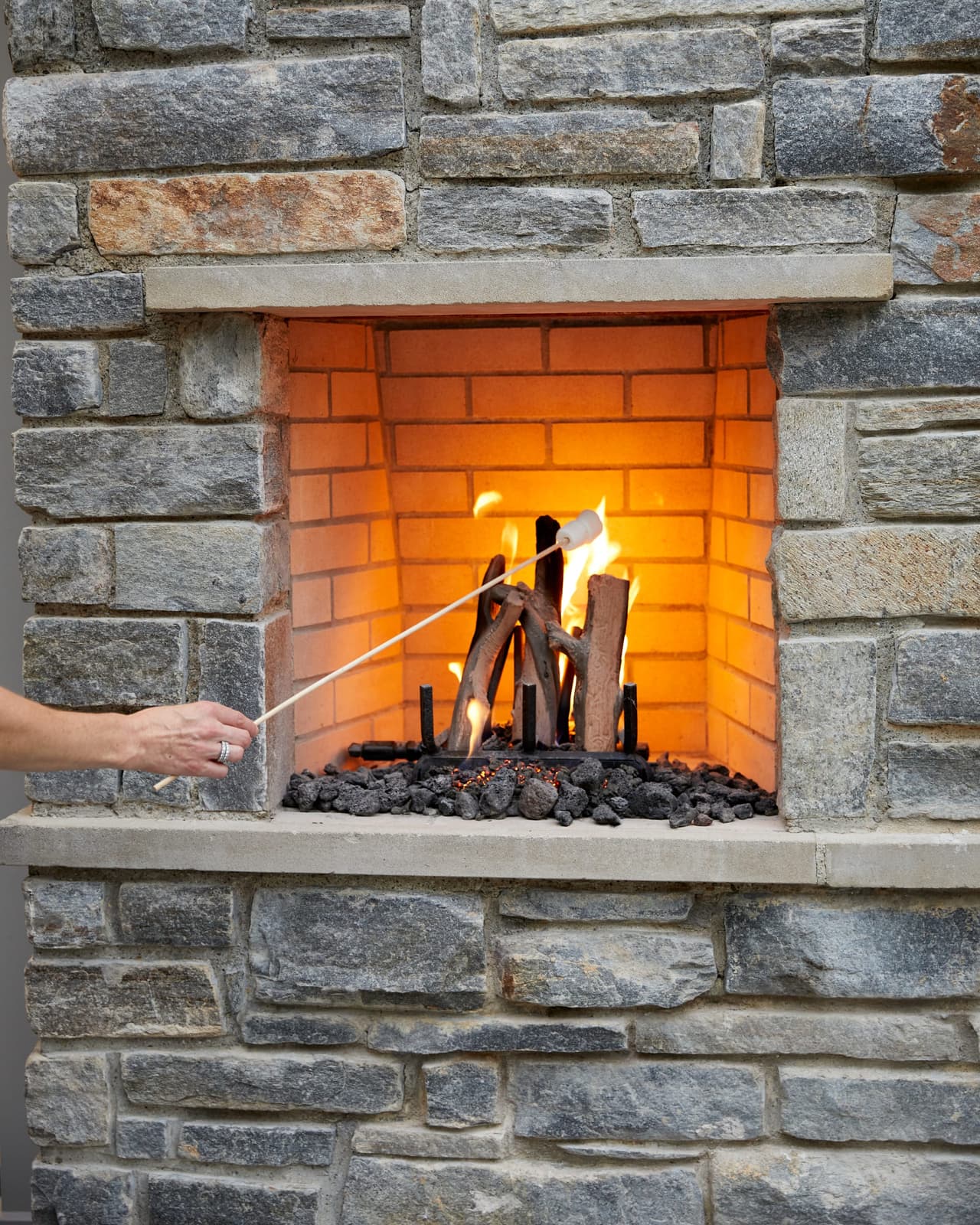 Stone outdoor fireplace lit for a s'mores station, with a marshmallow on a skewer, in a Westfield, NJ backyard