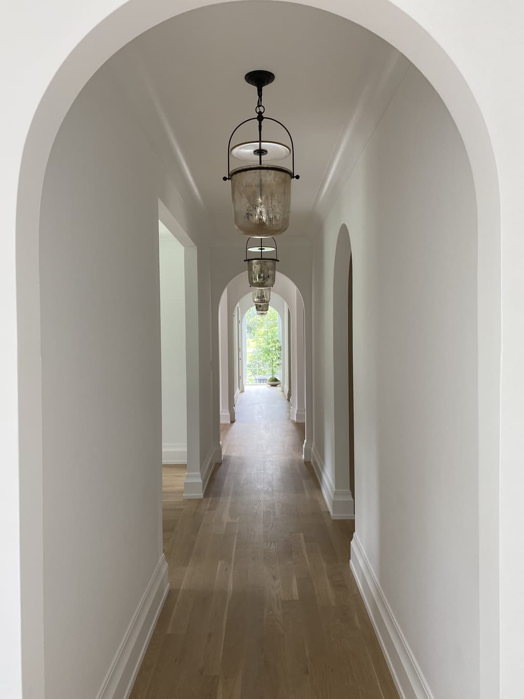 Two plaster arches down a hallway of a Westfield, NJ new-construction home, each with a glass bell lantern hung beneath it