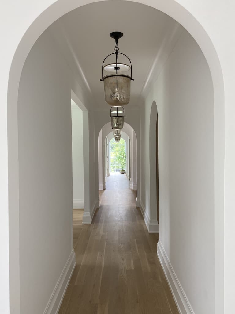 Two plaster arches down a hallway of a Westfield, NJ new-construction home, each with a glass bell lantern hung beneath it
