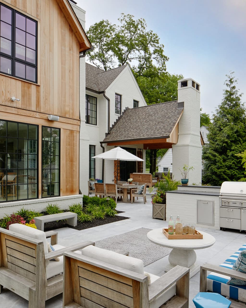 Backyard terrace with a built-in outdoor kitchen, teak seating, planters and an umbrella beside a new construction home in Westfield, NJ