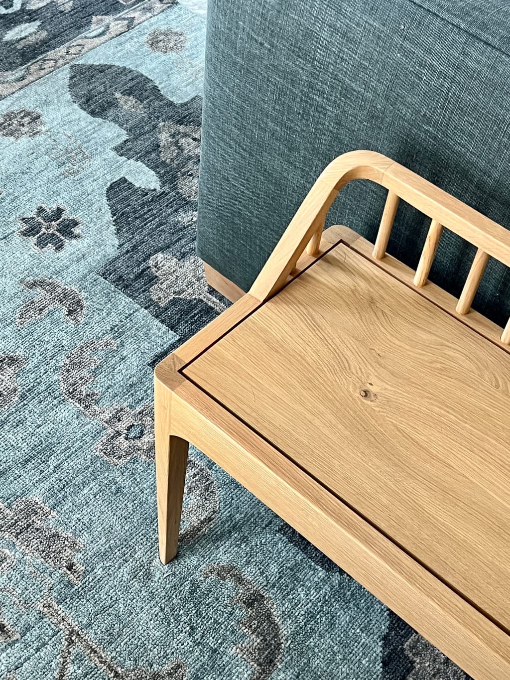 Oak spindle-back bench on a faded blue patterned rug at the foot of the bed in a Westfield, NJ home addition
