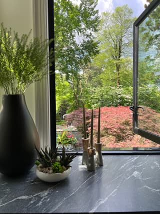 Black-framed casement swung open over a soapstone counter in a New Jersey home renovation, with a Japanese maple in the garden beyond