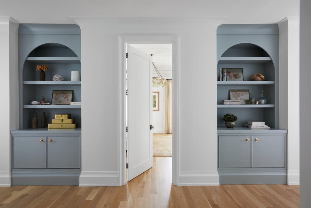 Hallway lined with pale blue arched built-in bookcases either side of a doorway in a Westfield, NJ new-construction home