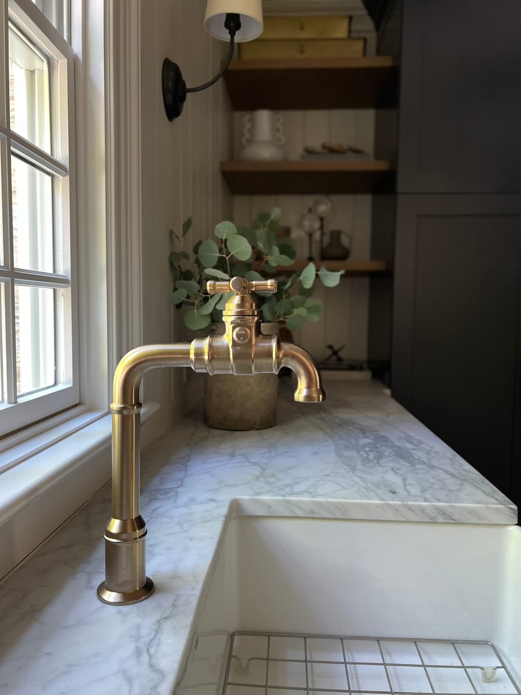 Unlacquered brass bridge tap over a marble apron sink below walnut open shelves in a New Jersey mudroom renovation