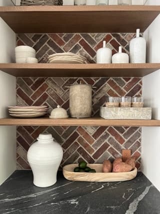 Oak open shelves set against a herringbone brick back wall above a soapstone counter in a New Jersey kitchen renovation