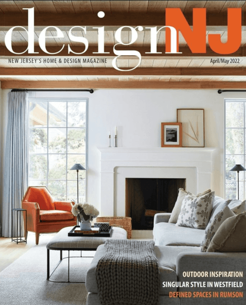 April/May 2022 cover of Design NJ, a living room with a white fireplace and an orange armchair, from its coverage of Michael Robert Construction