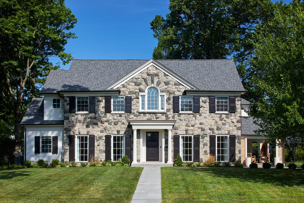 Front of a fieldstone and shingle Westfield, NJ home after a full renovation, with a pedimented entry, black shutters and a bluestone walk across the lawn
