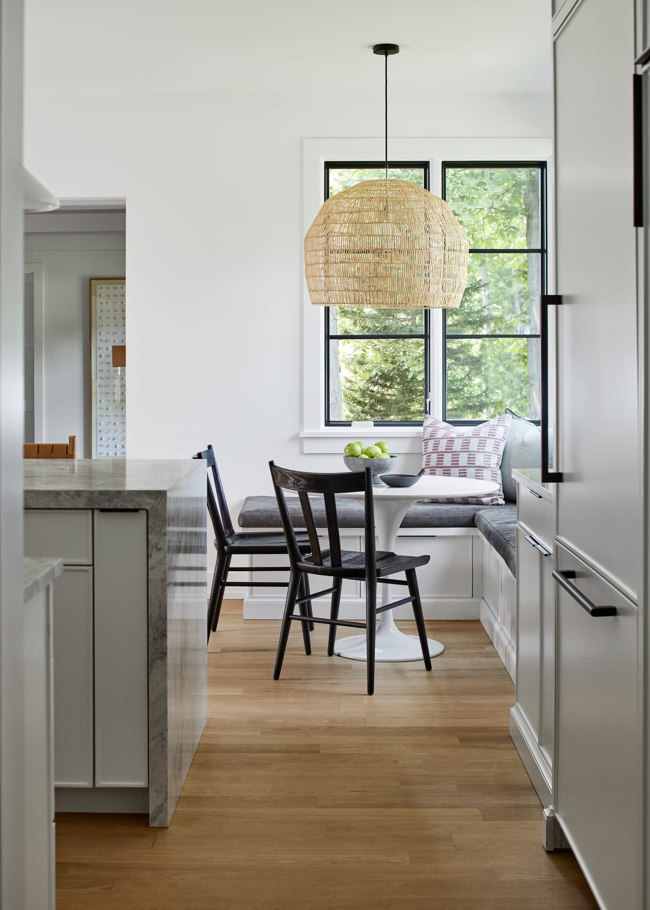 Breakfast nook off a white kitchen in Westfield, NJ, with a woven pendant over a round table, black spindle chairs and a window banquette