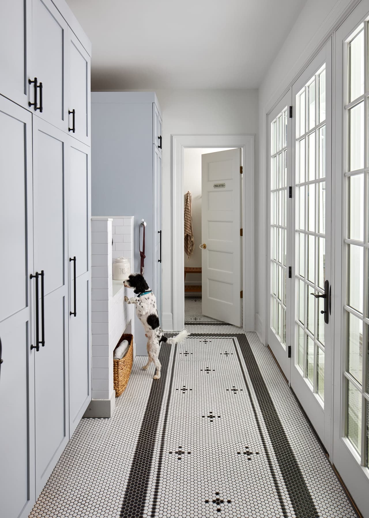 Mudroom corridor in a historic Westfield, NJ home, with white paneled doors, a patterned runner and French doors to the garden at the end