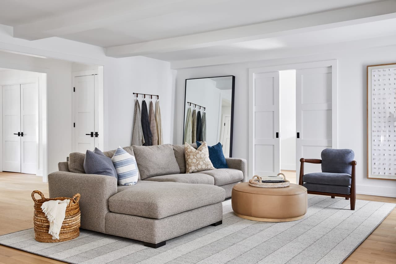 Family room of a Westfield, NJ home renovation, with a pale sectional and chaise on a flatweave rug, a leather sling chair and a bank of white doors behind