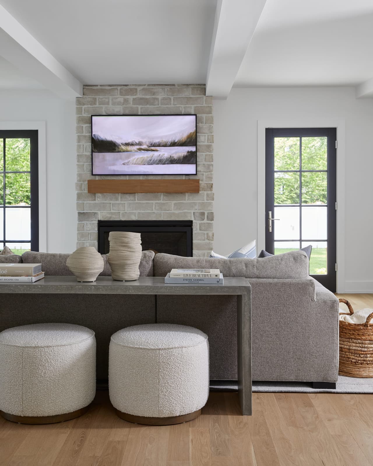 Stone fireplace with a floating mantel between two black-framed windows in a Westfield, NJ family room renovation, with boucle ottomans at the sofa