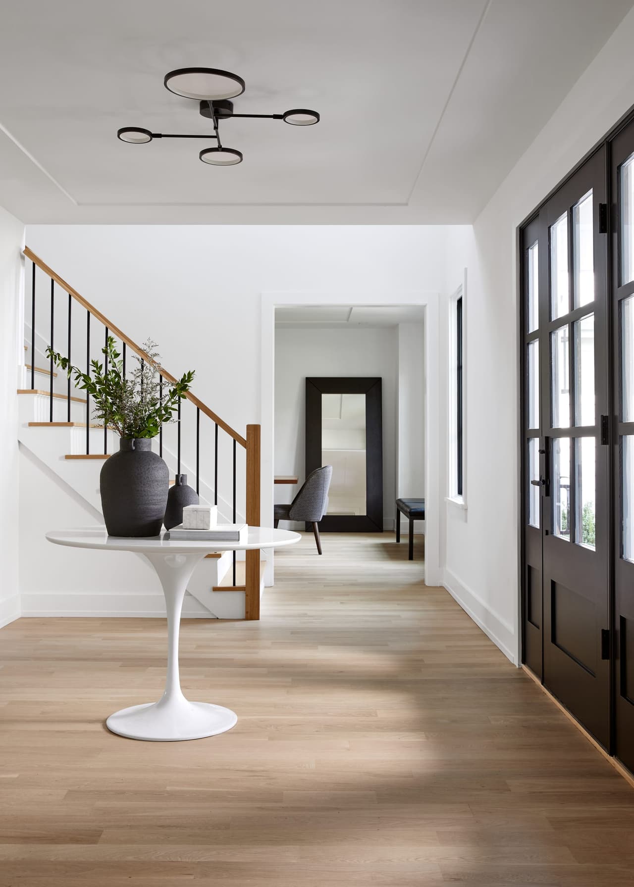 Foyer of a Westfield, NJ home renovation looking down the hall to the stair, with a marble pedestal table, black-framed doors and a two-ring ceiling light
