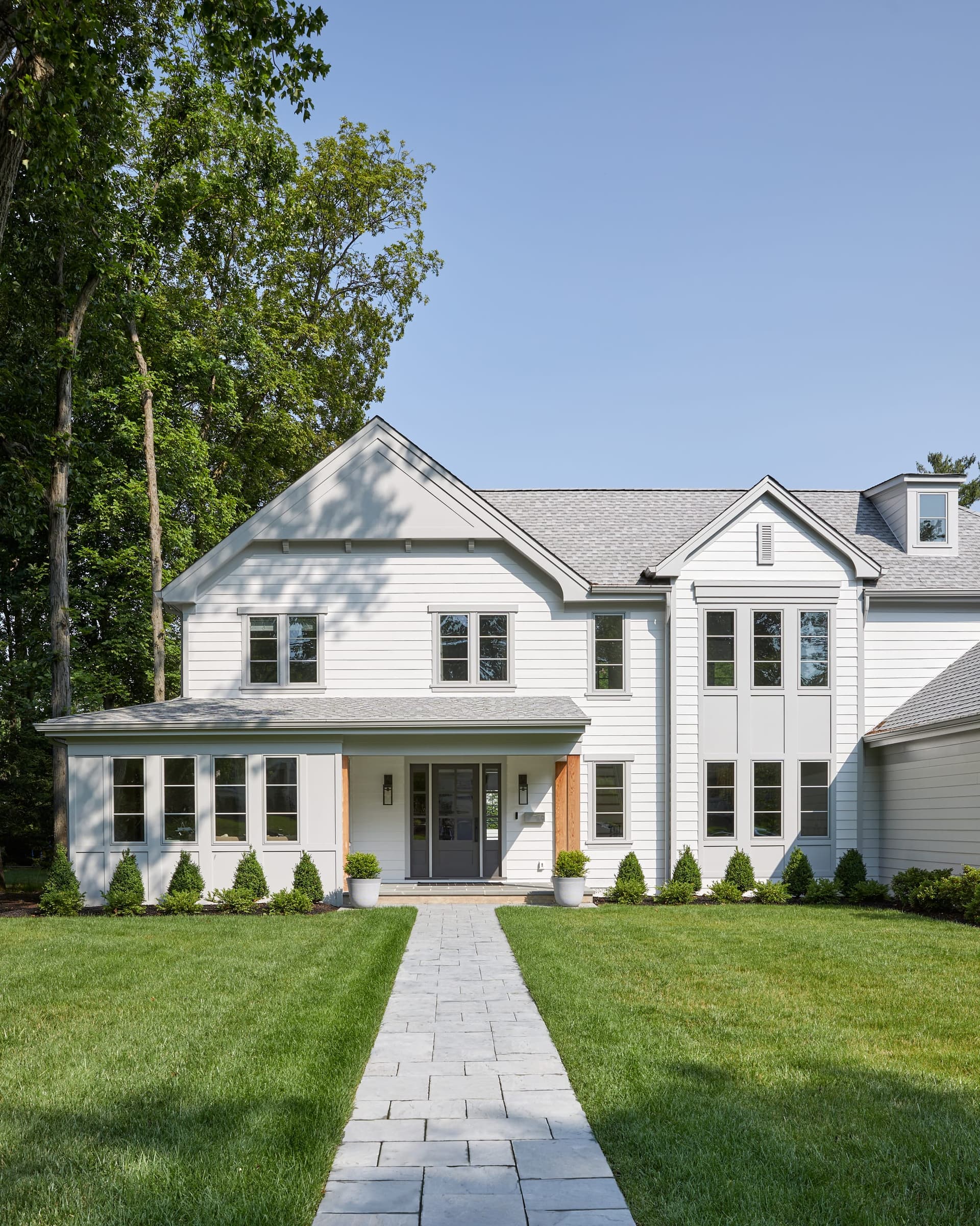 Front portico with cedar accents on a white Westfield, NJ home, approached by a paver walkway between clipped boxwood, by Michael Robert Construction