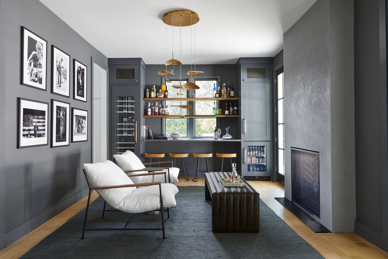 Lounge and bar in a Westfield, NJ home renovation, with charcoal walls, custom shelving over the counter, a gallery wall and a see-through fireplace, built by Michael Robert Construction