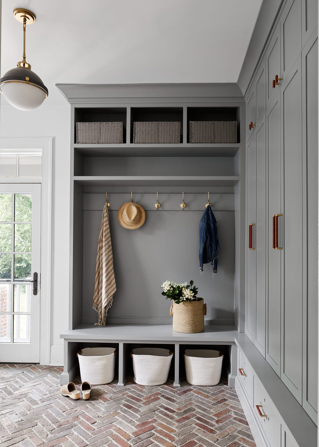 Mudroom of a historic Westfield, NJ home with gray built-in lockers, a bench over basket storage and herringbone brick floors