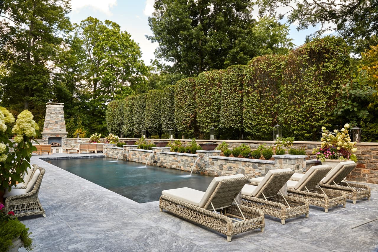 Rectangular pool on a bluestone terrace in a Westfield, NJ backyard, with woven loungers down one side and a tall clipped hedge enclosing the far end