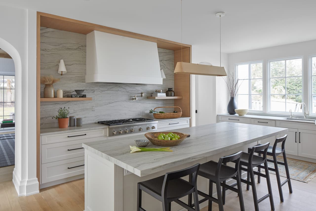 Kitchen with a plaster hood in a white oak surround, a marble island and black counter stools